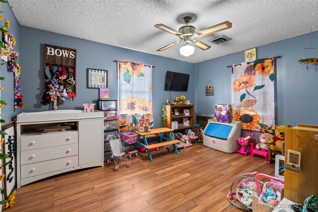 playroom with ceiling fan, light hardwood / wood-style floors, and a textured ceiling