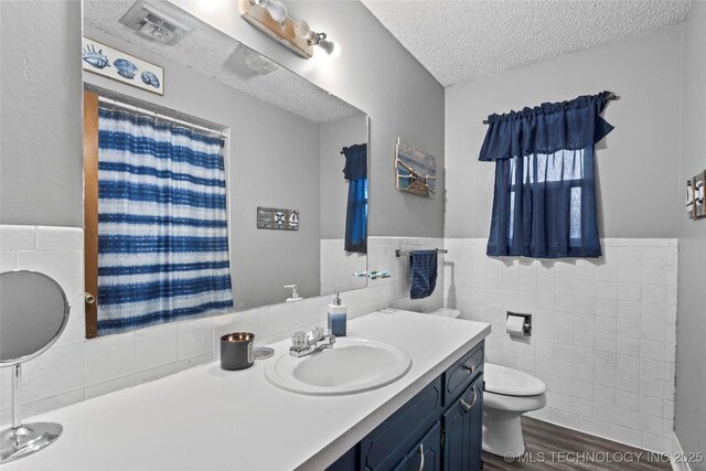 bathroom featuring vanity, a textured ceiling, tile walls, hardwood / wood-style floors, and toilet