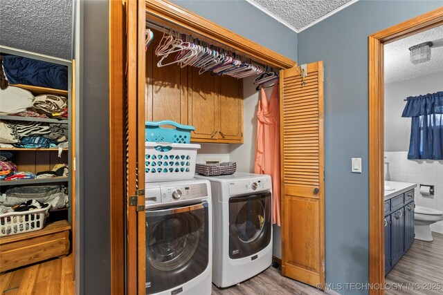 clothes washing area featuring washing machine and dryer, cabinets, a textured ceiling, and light wood-type flooring