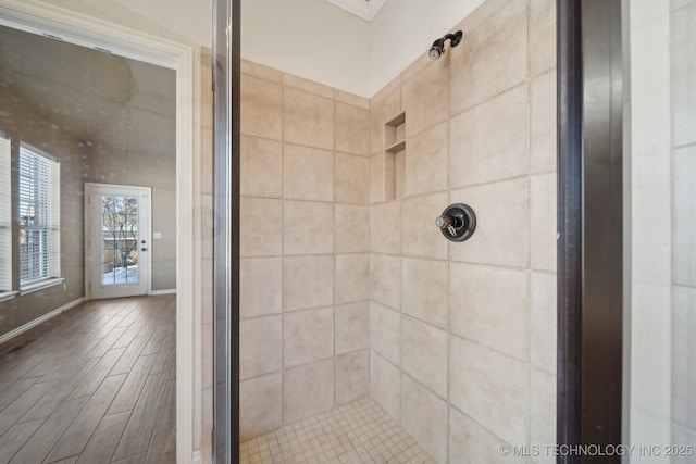 bathroom with a tile shower, wood finished floors, and baseboards