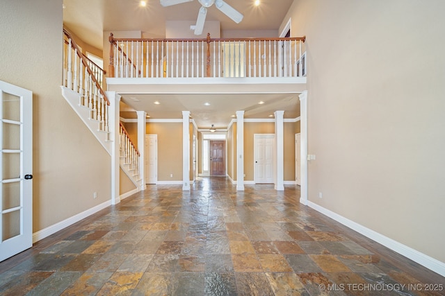 unfurnished living room featuring ceiling fan, ornate columns, ornamental molding, and a high ceiling