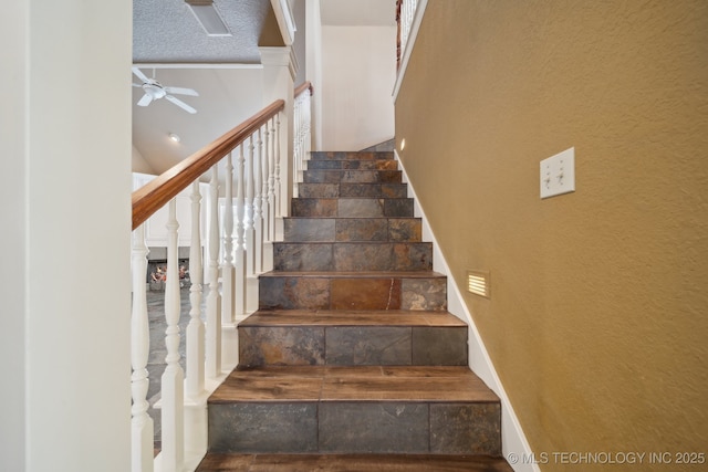 staircase with ceiling fan, lofted ceiling, and a textured ceiling