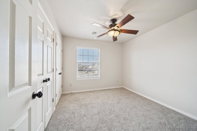 empty room featuring light colored carpet, baseboards, a ceiling fan, and visible vents