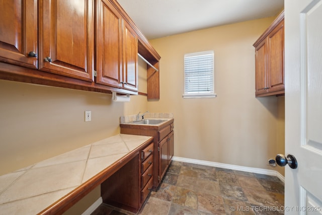 clothes washing area with stone finish flooring, baseboards, and a sink