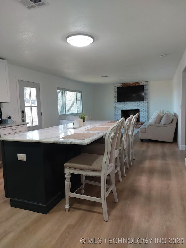 kitchen featuring white cabinetry, light stone countertops, a brick fireplace, wood-type flooring, and a kitchen bar