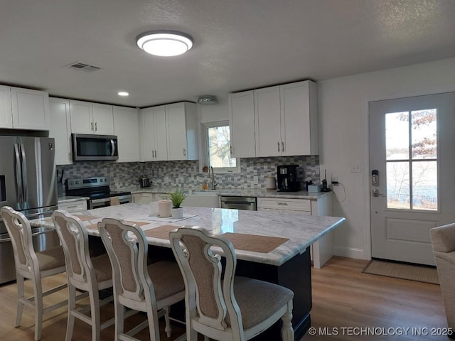 kitchen with a center island, light stone counters, white cabinetry, and stainless steel appliances