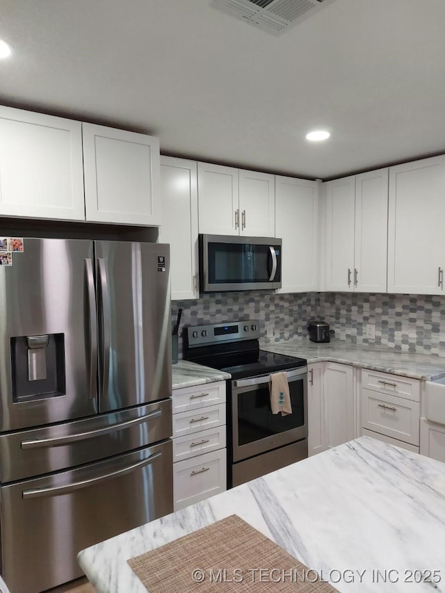 kitchen featuring light stone countertops, decorative backsplash, white cabinetry, and stainless steel appliances