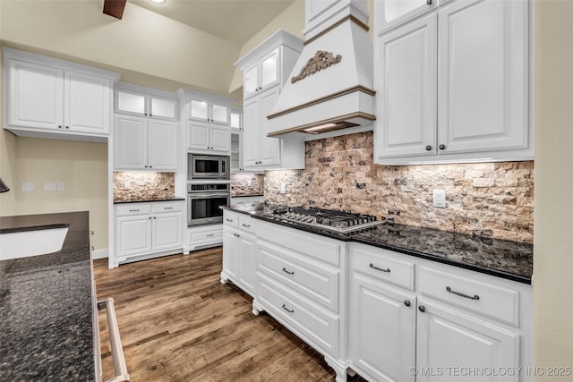 kitchen featuring white cabinets, custom range hood, appliances with stainless steel finishes, and dark stone counters