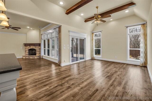 unfurnished living room featuring lofted ceiling with beams, dark hardwood / wood-style floors, a stone fireplace, and ceiling fan