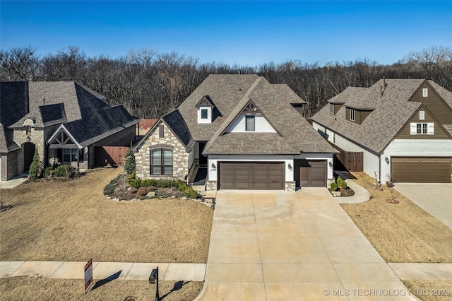 french country home featuring an attached garage, stone siding, driveway, and roof with shingles