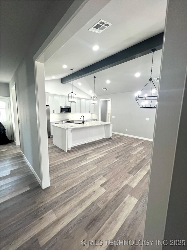 kitchen featuring hardwood / wood-style floors, an island with sink, decorative light fixtures, white cabinets, and appliances with stainless steel finishes