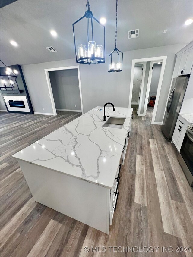 kitchen with light stone countertops, sink, pendant lighting, a center island with sink, and white cabinetry