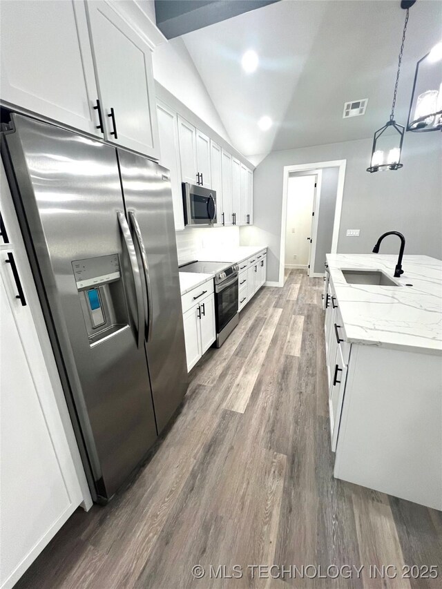 kitchen with stainless steel appliances, sink, pendant lighting, white cabinets, and lofted ceiling