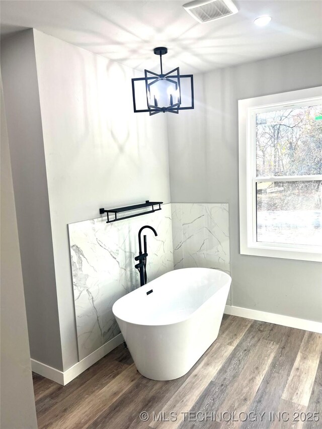 bathroom featuring wood-type flooring, a tub to relax in, and a notable chandelier