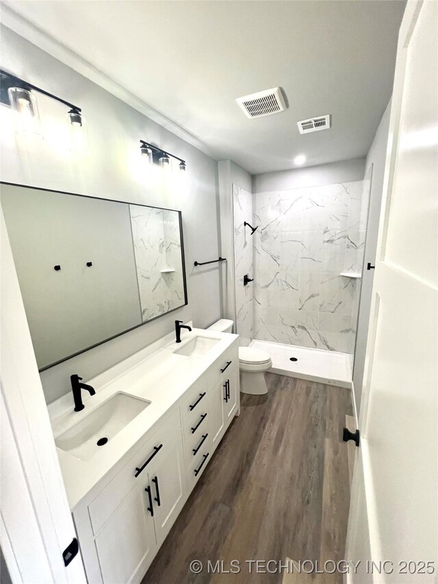 bathroom with toilet, hardwood / wood-style floors, vanity, and tiled shower