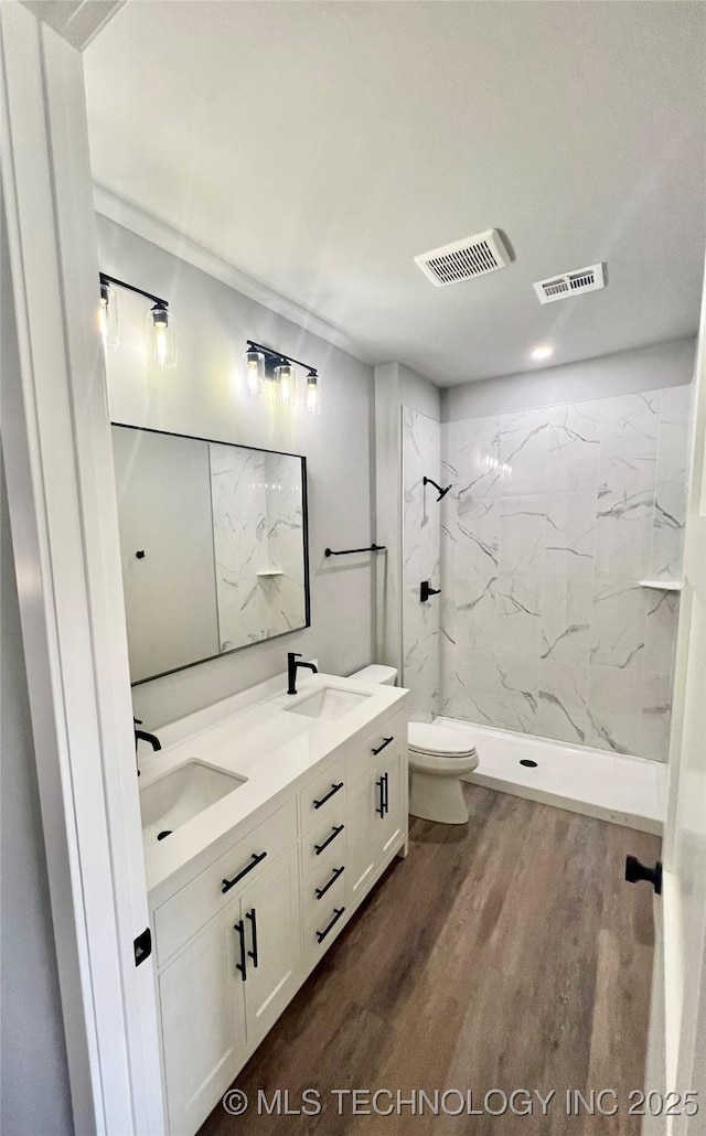 bathroom with toilet, vanity, wood-type flooring, and tiled shower