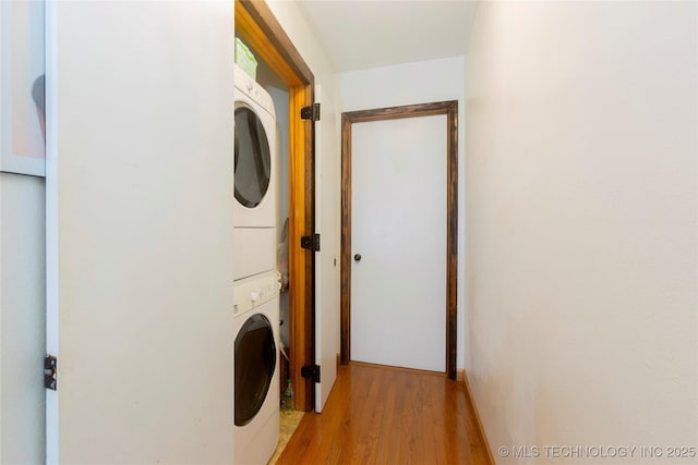 laundry room with stacked washing maching and dryer and light hardwood / wood-style flooring