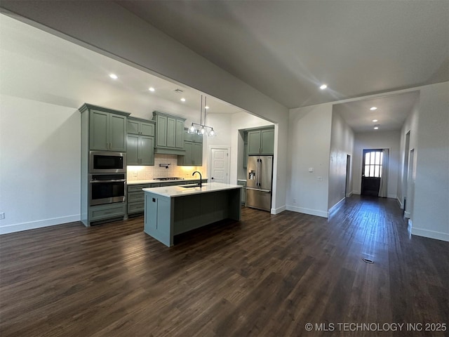 kitchen with sink, hanging light fixtures, stainless steel appliances, backsplash, and an island with sink