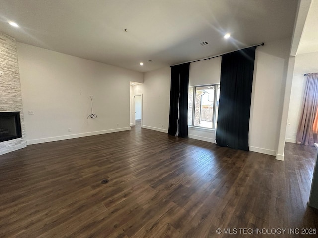 unfurnished living room featuring dark hardwood / wood-style flooring and a stone fireplace