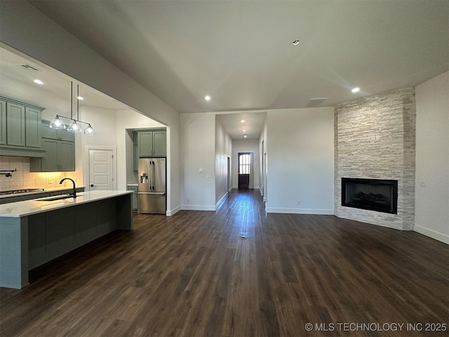 kitchen featuring pendant lighting, dark wood-type flooring, a stone fireplace, sink, and stainless steel fridge with ice dispenser