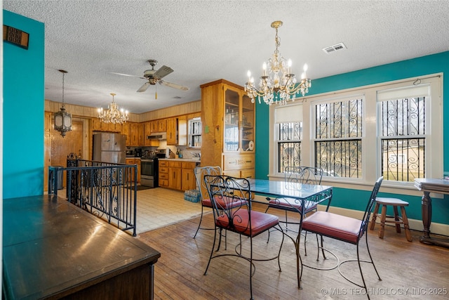 dining space with a textured ceiling, a wealth of natural light, light hardwood / wood-style floors, and ceiling fan with notable chandelier