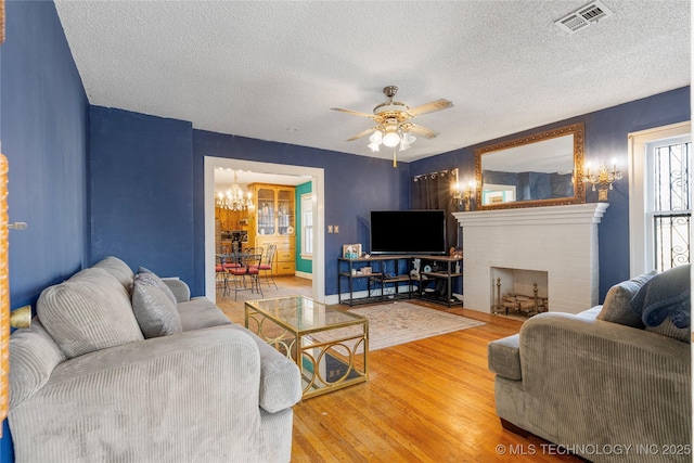 living room featuring ceiling fan with notable chandelier, a fireplace, wood-type flooring, and a textured ceiling