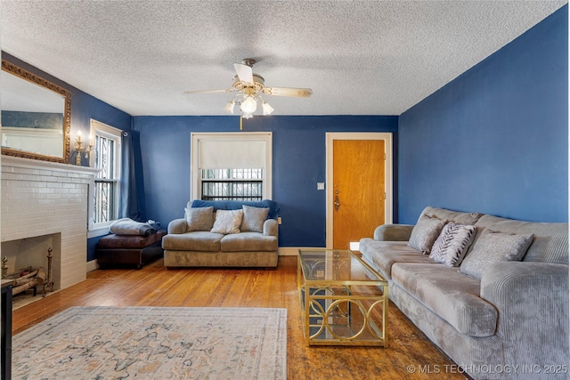 living room with ceiling fan, hardwood / wood-style floors, a textured ceiling, and a brick fireplace