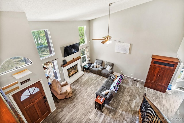 living room with ceiling fan, high vaulted ceiling, wood-type flooring, and a textured ceiling