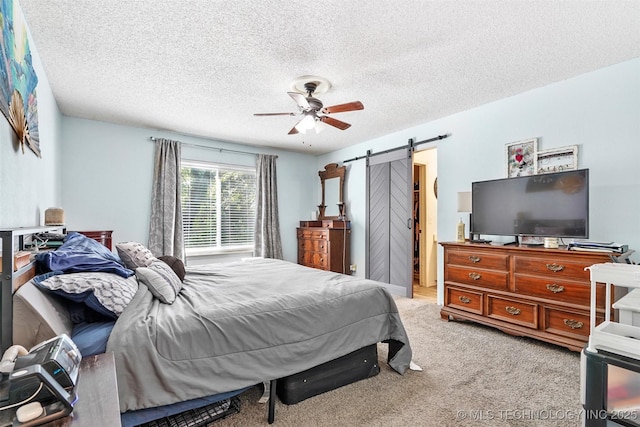 carpeted bedroom with a barn door, ceiling fan, and a textured ceiling