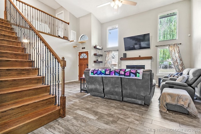 living room featuring ceiling fan, a high ceiling, and a brick fireplace