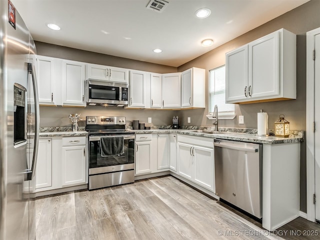 kitchen featuring sink, light stone countertops, appliances with stainless steel finishes, light hardwood / wood-style floors, and white cabinetry