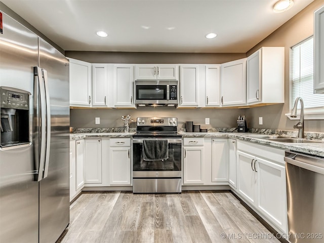 kitchen featuring light stone countertops, sink, light hardwood / wood-style floors, white cabinets, and appliances with stainless steel finishes