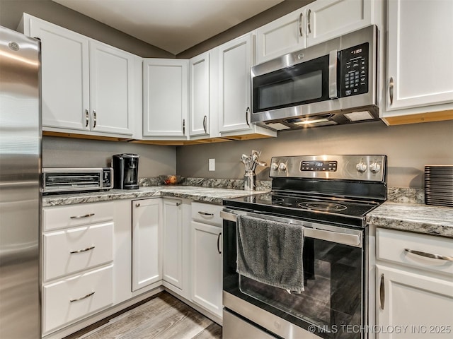 kitchen featuring light hardwood / wood-style floors, light stone countertops, white cabinetry, and stainless steel appliances