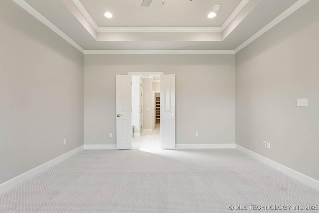 empty room with ceiling fan, a raised ceiling, light carpet, and crown molding