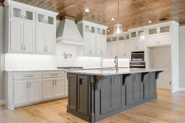 kitchen featuring white cabinetry, premium range hood, black microwave, and an island with sink