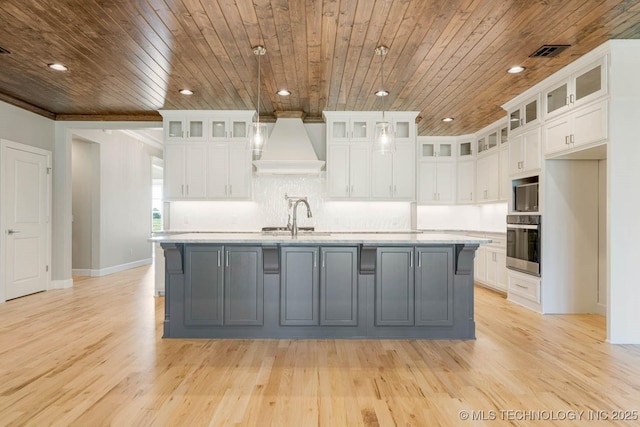 kitchen with a center island with sink, white cabinets, and custom range hood