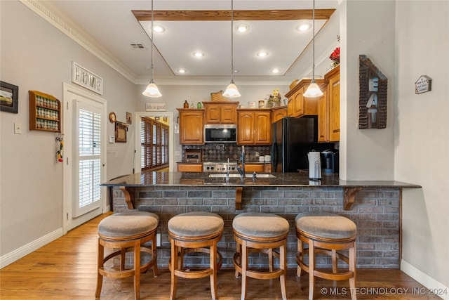 kitchen with a kitchen breakfast bar, black refrigerator, crown molding, decorative backsplash, and light wood-type flooring