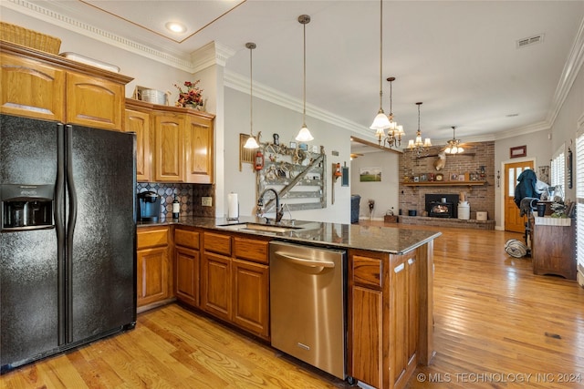 kitchen featuring light wood-type flooring, black refrigerator with ice dispenser, stainless steel dishwasher, sink, and hanging light fixtures