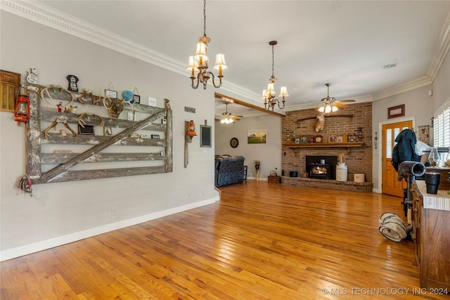 living room featuring a wood stove, hardwood / wood-style floors, ceiling fan with notable chandelier, and ornamental molding