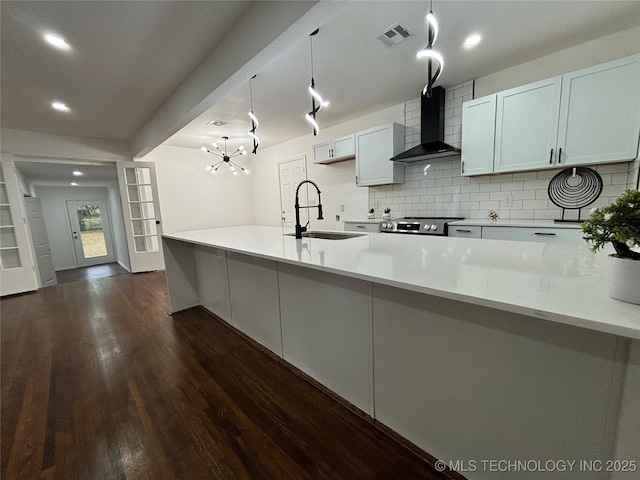 kitchen with white cabinetry, sink, wall chimney exhaust hood, backsplash, and pendant lighting