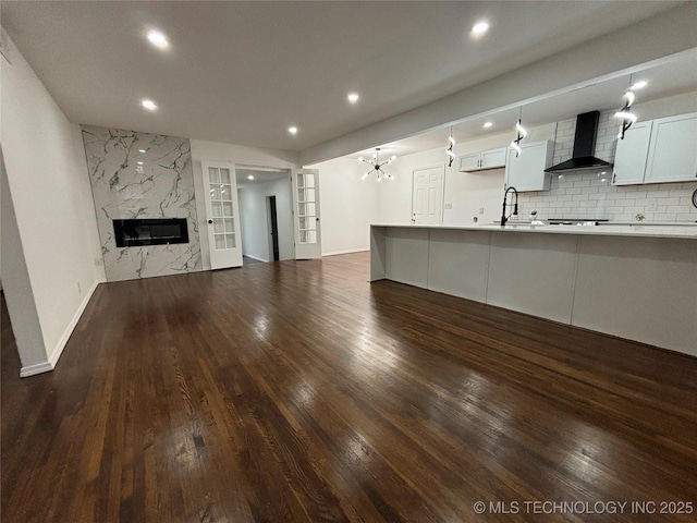 unfurnished living room with french doors, sink, a high end fireplace, dark hardwood / wood-style floors, and a notable chandelier