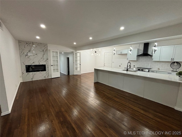 kitchen featuring white cabinetry, sink, french doors, wall chimney range hood, and tasteful backsplash