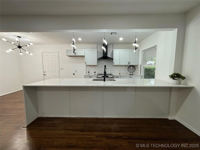 kitchen with backsplash, sink, wall chimney range hood, decorative light fixtures, and white cabinetry