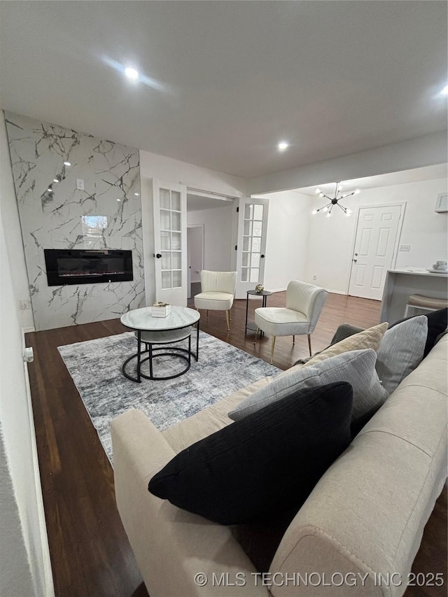 living room with built in features, dark hardwood / wood-style flooring, a high end fireplace, an inviting chandelier, and french doors