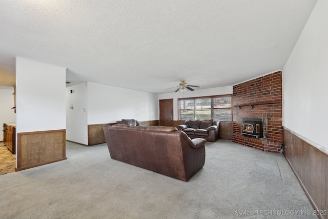 living room with wood walls, a wood stove, ceiling fan, a textured ceiling, and light colored carpet