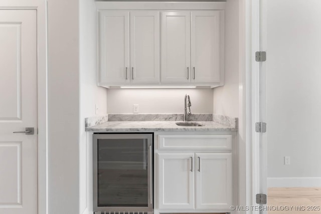 bar featuring light wood-type flooring, light stone counters, beverage cooler, sink, and white cabinetry