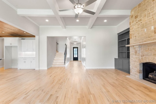 unfurnished living room with ceiling fan, coffered ceiling, a stone fireplace, built in features, and beamed ceiling