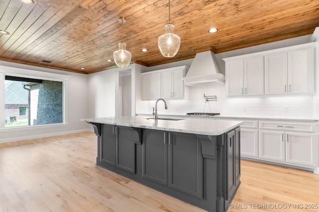 kitchen featuring sink, wooden ceiling, premium range hood, a center island with sink, and white cabinets