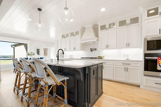 kitchen featuring light stone countertops, appliances with stainless steel finishes, premium range hood, sink, and hanging light fixtures