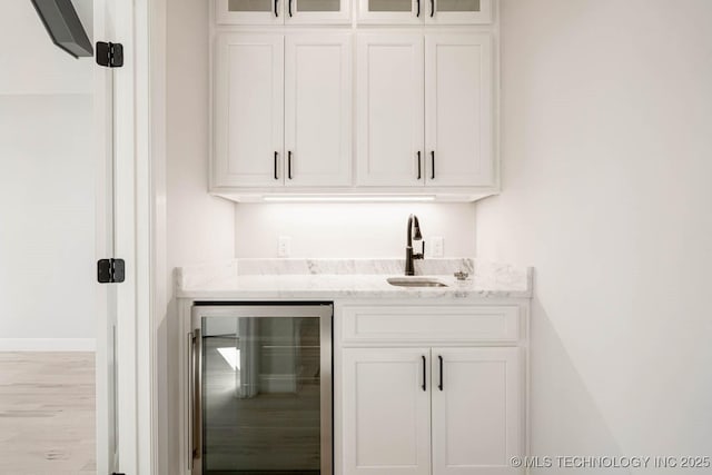 bar with white cabinetry, sink, wine cooler, light stone counters, and light hardwood / wood-style flooring